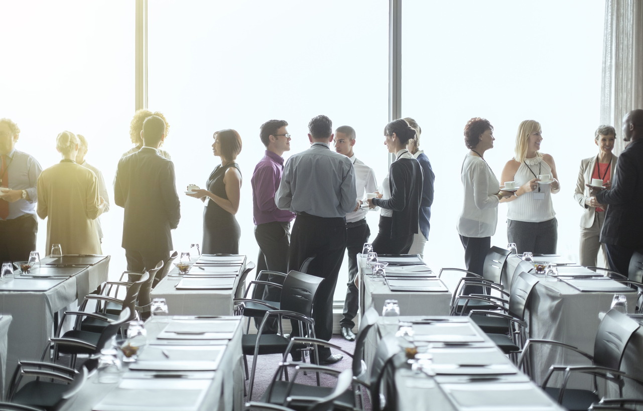 Group of people standing by windows of conference room, socializing during coffee break