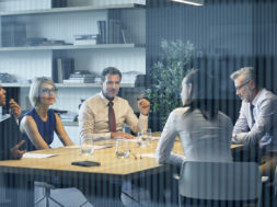 Coworkers communicating at desk seen through glass