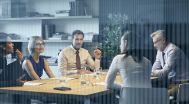 Coworkers communicating at desk seen through glass