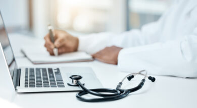 Laptop, stethoscope and doctor writing in notebook for research planning or medical tech innovation in hospital office. Healthcare medic worker, research strategy book notes and online communication