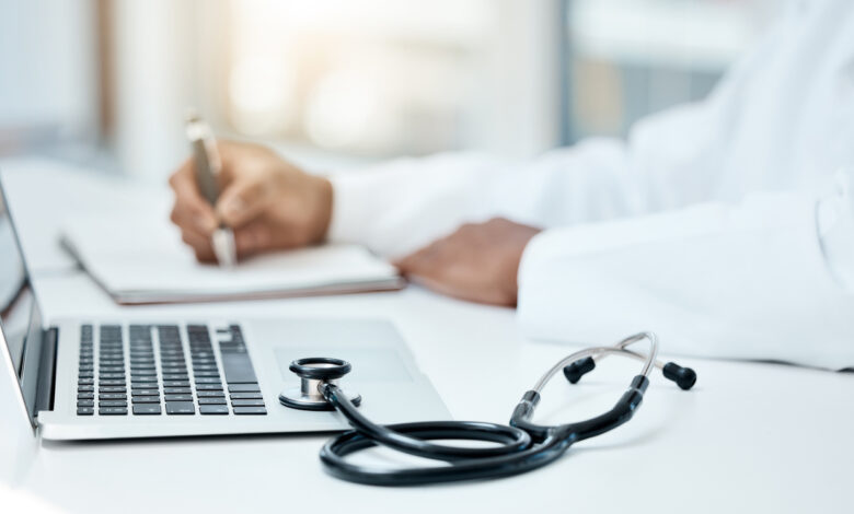 Laptop, stethoscope and doctor writing in notebook for research planning or medical tech innovation in hospital office. Healthcare medic worker, research strategy book notes and online communication