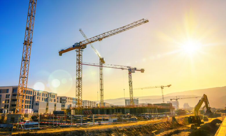 Large construction site including several cranes, with clear sky and the sun