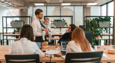 Father is holding his son. Infant baby is in the office where group of people are working together