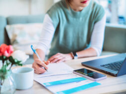 Young Asian women managing home finance using laptop & smartphone. She is working with household utility bill and calculating expenses at home.