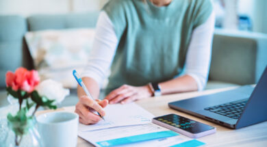 Young Asian women managing home finance using laptop & smartphone. She is working with household utility bill and calculating expenses at home.