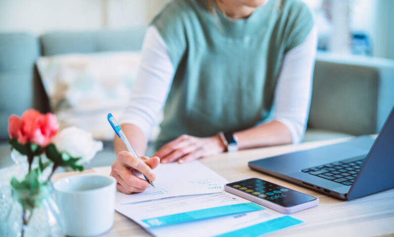 Young Asian women managing home finance using laptop & smartphone. She is working with household utility bill and calculating expenses at home.