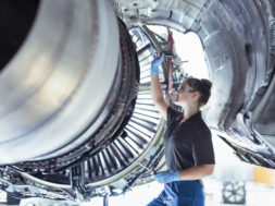 Female apprentice aircraft maintenance engineer work underneath jet engine