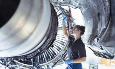 Female apprentice aircraft maintenance engineer work underneath jet engine