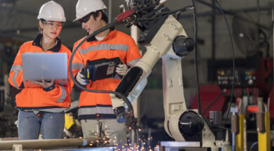 Two Industrials Engineer holding the Laptop Computer examining the operating Robotic welding Machine in the factory.