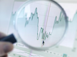 Investor analysing line graph on computer screen with magnifying glass