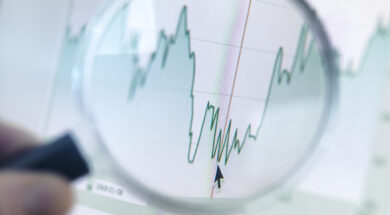 Investor analysing line graph on computer screen with magnifying glass