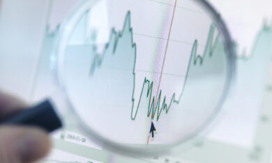 Investor analysing line graph on computer screen with magnifying glass