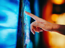 Close up of woman’s hand touching illuminated and multi-coloured LED display screen, connecting to the future. People, lifestyle and technology