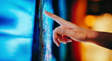 Close up of woman’s hand touching illuminated and multi-coloured LED display screen, connecting to the future. People, lifestyle and technology