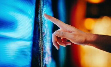 Close up of woman’s hand touching illuminated and multi-coloured LED display screen, connecting to the future. People, lifestyle and technology