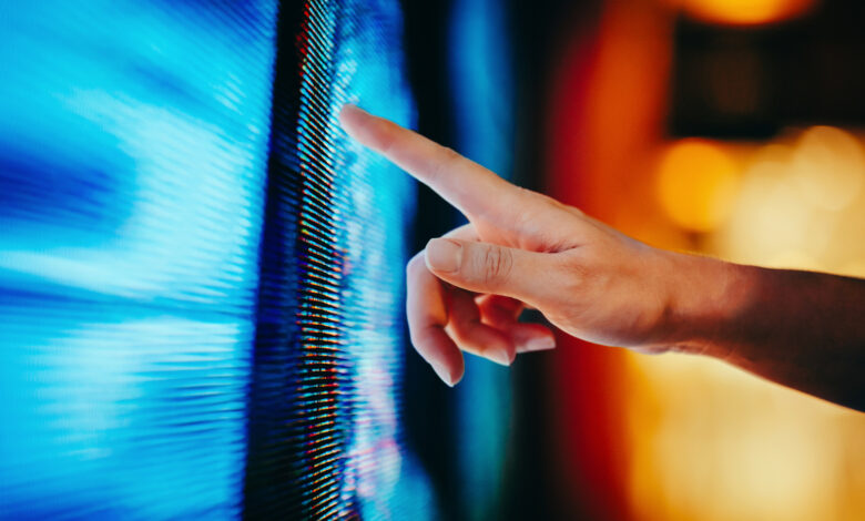 Close up of woman’s hand touching illuminated and multi-coloured LED display screen, connecting to the future. People, lifestyle and technology
