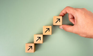 Business goal growth management, new objective, success plan, leadership concepts. Businessman hand arranged wooden cube blocks with rising arrow icon isolated on green background, minimalist style.