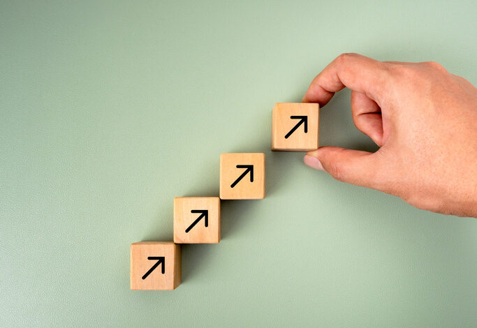 Business goal growth management, new objective, success plan, leadership concepts. Businessman hand arranged wooden cube blocks with rising arrow icon isolated on green background, minimalist style.