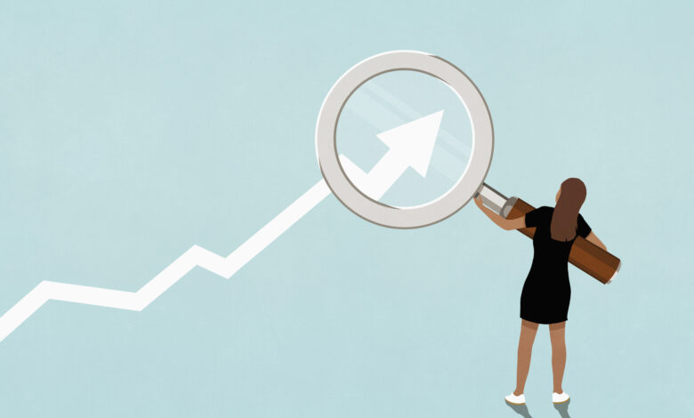 Woman holding magnifying glass over ascending graph arrow on blue background