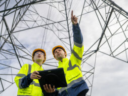 Electrical engineers inspecting high voltage power lines using digital tablet