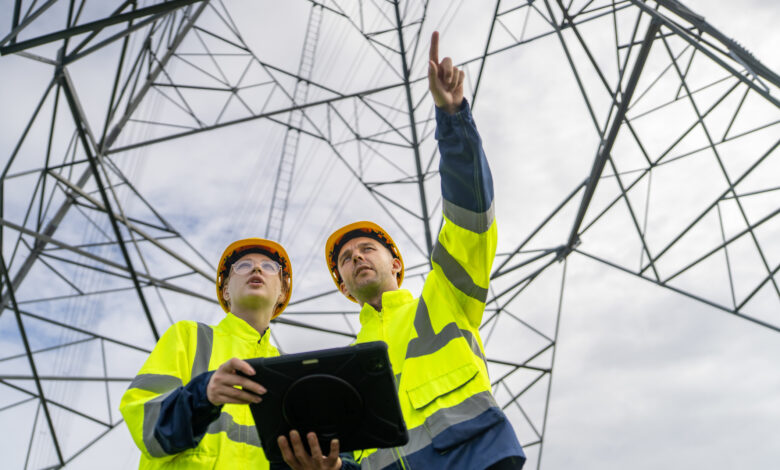 Electrical engineers inspecting high voltage power lines using digital tablet
