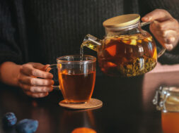 Female hand pouring tea into transparent cup. Glass teapot with fruit leaf tea. Life style cozy home interior photo. Morning refreshment concept