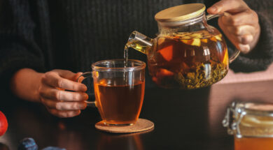 Female hand pouring tea into transparent cup. Glass teapot with fruit leaf tea. Life style cozy home interior photo. Morning refreshment concept