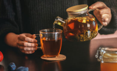 Female hand pouring tea into transparent cup. Glass teapot with fruit leaf tea. Life style cozy home interior photo. Morning refreshment concept