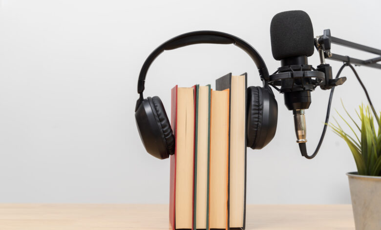 Headphones on books with microphone on desk symbolizing audiobook, podcast, learning and modern education